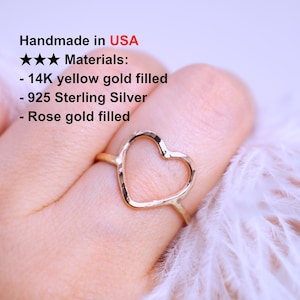 May include: A gold heart-shaped ring on a finger. The ring is made of 14K yellow gold filled, 925 Sterling Silver, or rose gold filled.