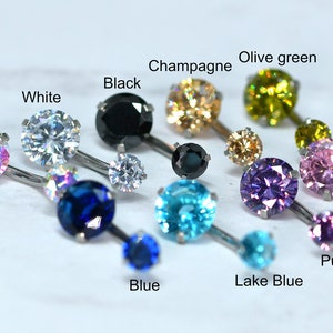 May include: A selection of belly button rings in colours such as rainbow, white, black, champagne, olive green, blue, lake blue, purple, and pink. Each ring has a large, round gemstone and a smaller accent stone.
