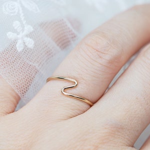 Puede incluir: Un delicado anillo de oro con un dise&ntilde;o en zigzag &uacute;nico. El anillo es fino y minimalista, con un patr&oacute;n continuo en forma de onda. La joya se muestra en un dedo, destacando su elegante simplicidad. El dise&ntilde;o del anillo es moderno y elegante.