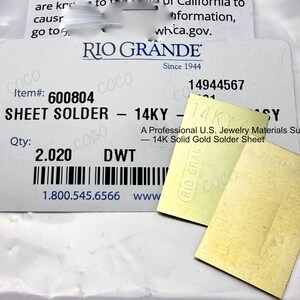 Puede incluir: Dos l&aacute;minas de soldadura de oro macizo de 14K se muestran junto a una tarjeta blanca con texto. La tarjeta dice "RIO GRANDE Since 1944" e incluye detalles del art&iacute;culo: "SHEET SOLDER - 14KY - 2.020 DWT". La imagen es de suministros para la fabricaci&oacute;n de joyas.