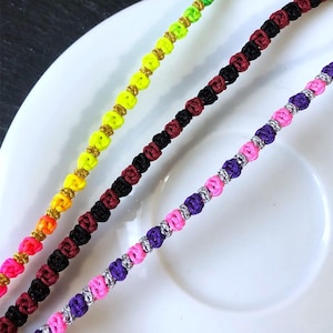 Peut inclure: Quatre bracelets d'amitié colorés. Les bracelets sont faits de fil noué aux couleurs vives : rose, jaune, vert et bleu. Chaque bracelet a de petits accents dorés ou argentés. Les bracelets sont présentés sur une assiette blanche.