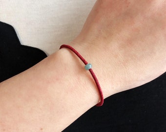 May include: A red string bracelet with a light blue bead.