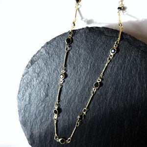 Può includere: Una collana a catena dorata con pietre rotonde nere. La collana è su una superficie di ardesia nera.