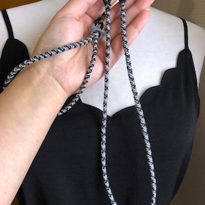 Peut inclure: Un collier en cordon tressé noir et blanc avec un fermoir en métal argenté.