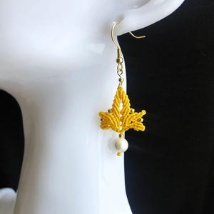 Könnte beinhalten: Gelbe geknüpfte Ohrringe mit einem Perlenanhänger. Die Ohrringe sind mit einem goldfarbenen Metallhaken gefertigt.