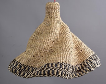 Pode incluir: Um candeeiro pendente tecido com uma cor palha natural e uma borda com padrão preto e branco. O candeeiro tem a forma de um sino e pendura num cordão vermelho.
