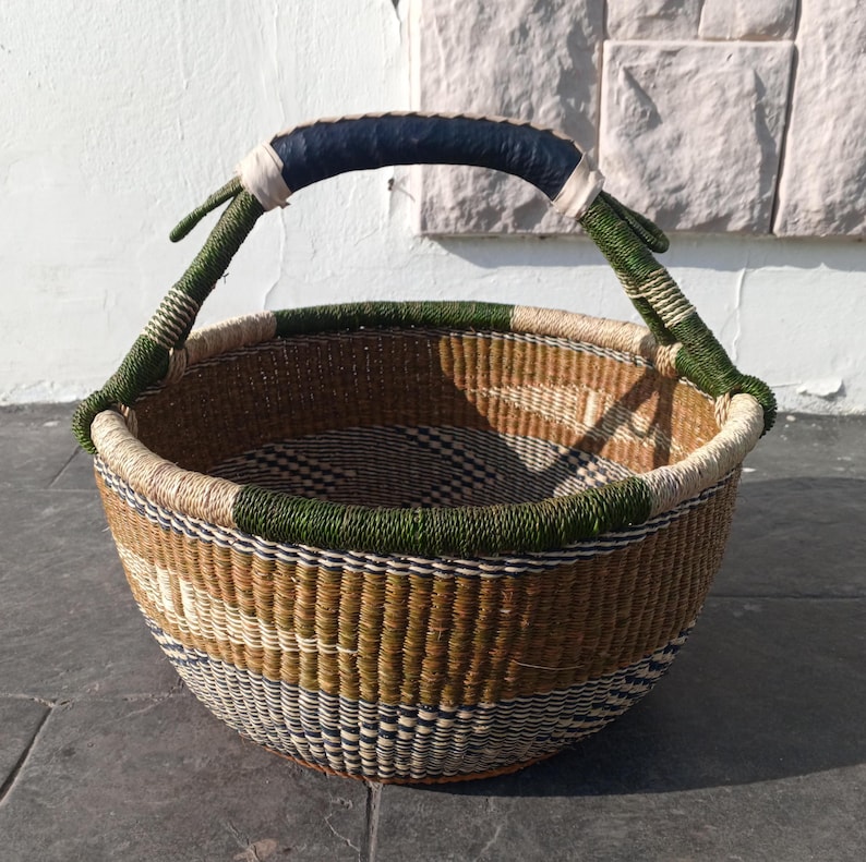 Puede incluir: Una cesta grande tejida con un patr&oacute;n verde, negro y blanco. La cesta tiene un asa de cuero negro resistente.