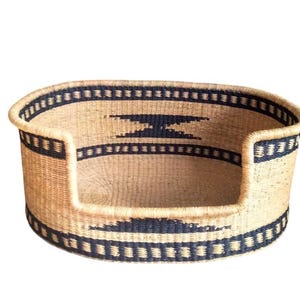 May include: A woven dog bed with a black and tan pattern. The bed is oval shaped and has a raised rim.