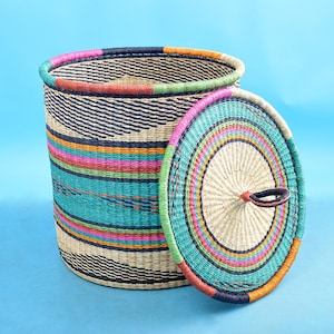 May include: A woven storage basket with a lid, featuring a colorful striped pattern in shades of pink, orange, teal, and black. The lid has a circular design with a woven handle.