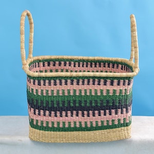 Könnte beinhalten: Ein geflochtener Aufbewahrungskorb mit zwei Griffen. Der Korb ist aus natürlichen Materialien gefertigt und hat ein geometrisches Muster in Pink, Grün und Schwarz.