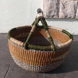 Puede incluir: Una cesta grande, redonda y tejida con un patr&oacute;n verde y marr&oacute;n. La cesta tiene un asa resistente hecha de cuero y material verde tejido.