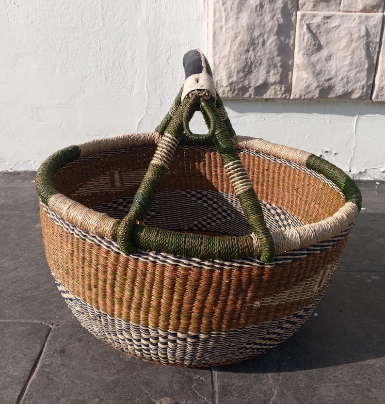 Puede incluir: Una cesta grande, redonda y tejida con un patr&oacute;n verde y marr&oacute;n. La cesta tiene un asa resistente hecha de cuero y material verde tejido.