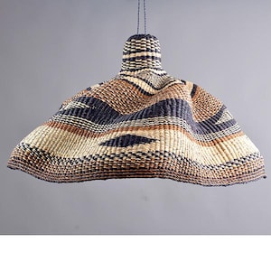 Pode incluir: Uma lumin&aacute;ria pendente tecida com uma sombra larga e flare. A sombra &eacute; feita de fibras naturais em tons de bege, marrom e azul marinho, criando um padr&atilde;o listrado. A lumin&aacute;ria &eacute; suspensa por um cabo escuro e tem um topo cil&iacute;ndrico.