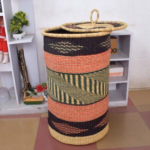 May include: A large, woven storage basket with a lid. The basket is made of natural materials and has a black, green, and red geometric pattern. The lid has a handle.