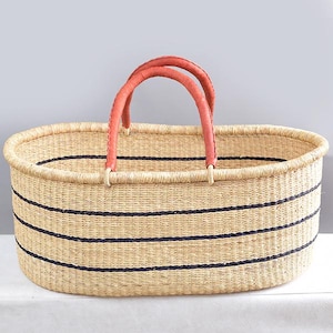 May include: Oval woven basket with black stripes and red leather handles. The basket is made from natural fibres. The basket is a light tan colour and is suitable for storage or decoration. The basket measures approximately 60cm in length.