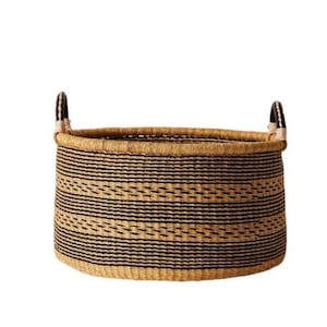May include: A round woven basket with a natural beige base and horizontal black stripes. The basket has two sturdy handles and is suitable for storage or decorative purposes. The basket is made of natural materials.