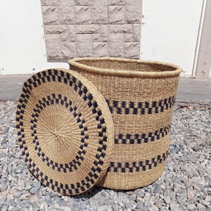 May include: A large, round, woven storage basket with a lid. The basket is made of natural materials and has black and white stripes. The lid has a similar pattern.