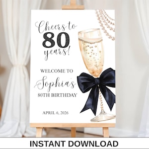 Könnte beinhalten: Ein weißes Schild auf einer Staffelei mit dem Text "Cheers to 80 years! Welcome to Sophia's 80th Birthday April 6, 2026." Ein Champagnerglas, eine schwarze Schleife und eine Perlenkette sind auf dem Schild abgebildet. Der Text "Instant Download" steht unten.