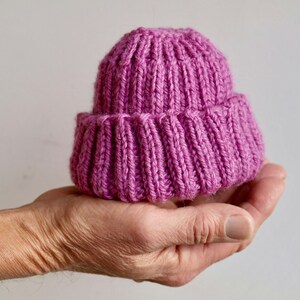 Puede incluir: Un gorro de punto pequeño de color rosa que se sostiene en una mano.