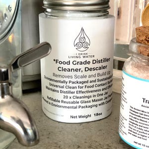 以下が含まれることがあります： 銀色の蓋が付いた白い瓶に「フードグレードディスティラークリーナー、デスケーラー」とラベルが貼られており、「I Drink Living Water」と「Net Weight 18oz」の文字が書かれています。