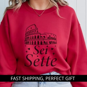 May include: Red sweatshirt featuring a black graphic of the Colosseum and the words "Sei Sette". The design includes hearts and stars. The sweatshirt is a solid red color.