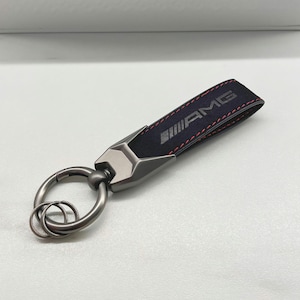 Porte-clés Mercedes-Benz AMG noir avec surpiqûres rouges, en cuir Alcantara. Porte-clés Mercedes-Benz AMG en cuir Alcantara de haute qualité.