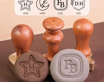 May include: Three wooden wax seal stamps with turned handles and brass heads. Two circular wax impressions are displayed in front, one brown with a star and letter H, and one gray with the letters FB. Above are four black line art design options.