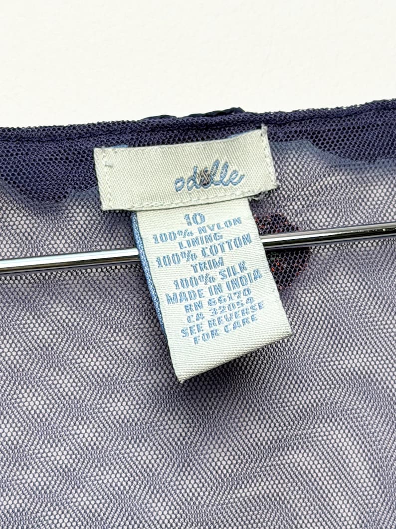May include: A dark blue mesh garment with a white clothing tag featuring the brand name Odille. The tag displays size 10, 100% nylon, 100% cotton lining, 100% silk trim, Made in India, RN 56170, CA 32054, and the text See Reverse For Care.