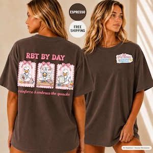 Op de afbeelding: Een donkerbruin t-shirt met korte mouwen en een afbeelding op de achterkant met drie panelen van getekende eenden en de tekst RBT BY DAY en reinforce & embrace the quacks. Op de borst staat een klein logo met de tekst Silly Goose RBT.