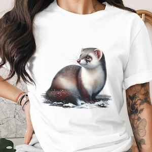 Puede incluir: Camiseta blanca con una ilustración detallada de un hurón. El hurón tiene pelaje marrón, blanco y negro, sobre un fondo nevado. La camiseta es de estilo casual, adecuada para el uso diario.