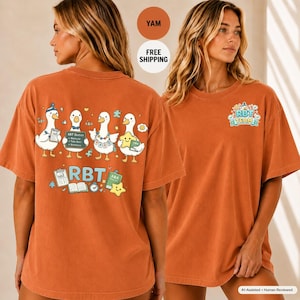 May include: A burnt orange short-sleeve t-shirt featuring a graphic on the back of four cartoon ducks with various items like clipboards and stars, with the text RBT. The front chest area displays a smaller graphic with the text RBT TEAM.