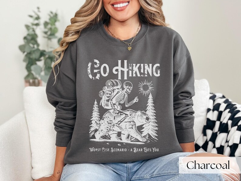 Woman wearing grey Go Hiking Worst Case Scenario A Bear Kills You, Funny Camping Sweater featuring a skeleton on a bear. Perfect for outdoor enthusiasts and camper gifts. Ideal for Halloween and summer vacation.