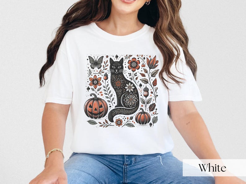 Woman wearing white Black Cat Halloween shirt featuring a spooky black cat, pumpkins, fall leaves, and flowers. Perfect for autumn and spooky season. Ideal for Halloween parties or as a cat lover gift with a vintage floral and witchy aesthetic.