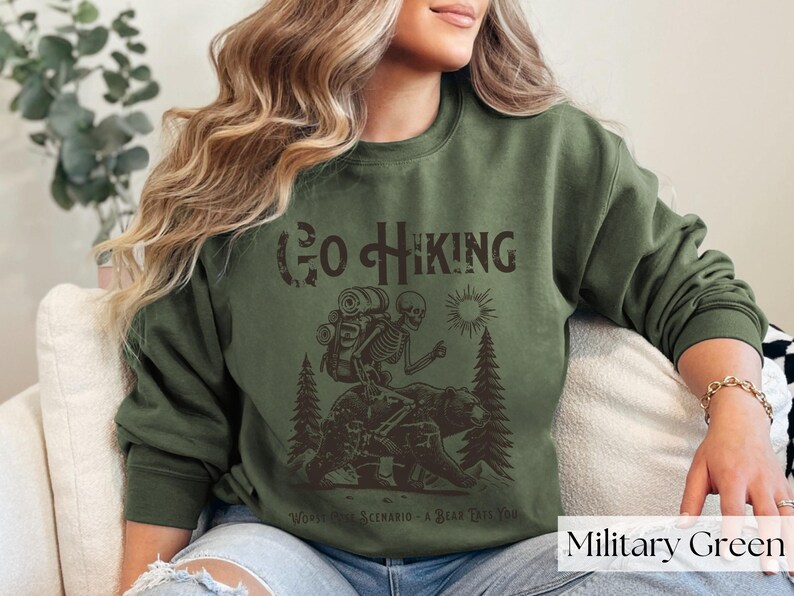 Woman wearing green Go Hiking Worst Case Scenario A Bear Kills You, Funny Camping Sweater featuring a skeleton on a bear. Perfect for outdoor enthusiasts and camper gifts. Ideal for Halloween and summer vacation.