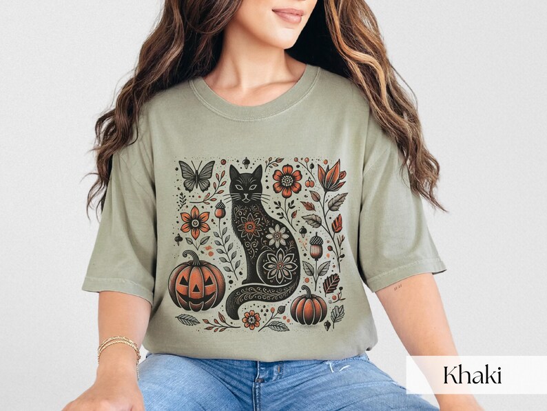 Woman wearing beige Black Cat Halloween shirt featuring a spooky black cat, pumpkins, fall leaves, and flowers. Perfect for autumn and spooky season. Ideal for Halloween parties or as a cat lover gift with a vintage floral and witchy aesthetic.