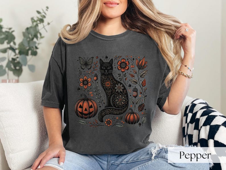 Woman wearing Black Cat Halloween shirt featuring a spooky black cat, pumpkins, fall leaves, and flowers. Perfect for autumn and spooky season. Ideal for Halloween parties or as a cat lover gift with a vintage floral and witchy aesthetic.