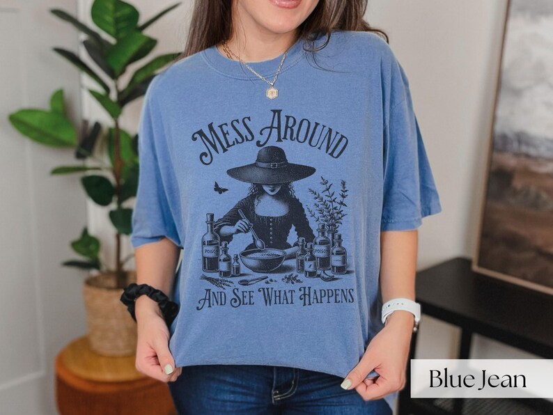Woman wearing blue Halloween Witch T-Shirt featuring Mess Around And See What Happens and a Witch Making Poison graphic. Perfect funny Halloween tee for a witchy aesthetic, spooky season, or a witch costume. Womens villain shirt for Halloween.
