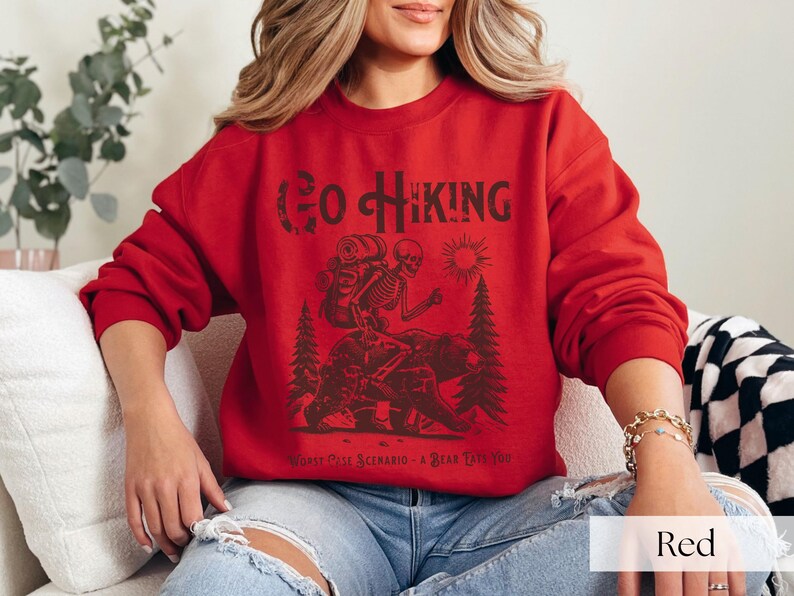 Woman wearing red Go Hiking Worst Case Scenario A Bear Kills You, Funny Camping Sweater featuring a skeleton on a bear. Perfect for outdoor enthusiasts and camper gifts. Ideal for Halloween and summer vacation.
