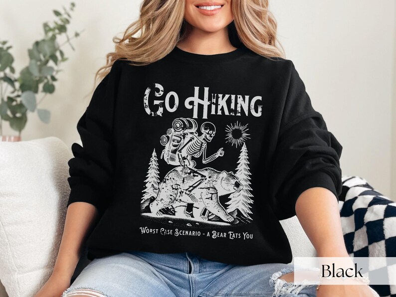 Woman wearing black Go Hiking Worst Case Scenario A Bear Kills You, Funny Camping Sweater featuring a skeleton on a bear. Perfect for outdoor enthusiasts and camper gifts. Ideal for Halloween and summer vacation.