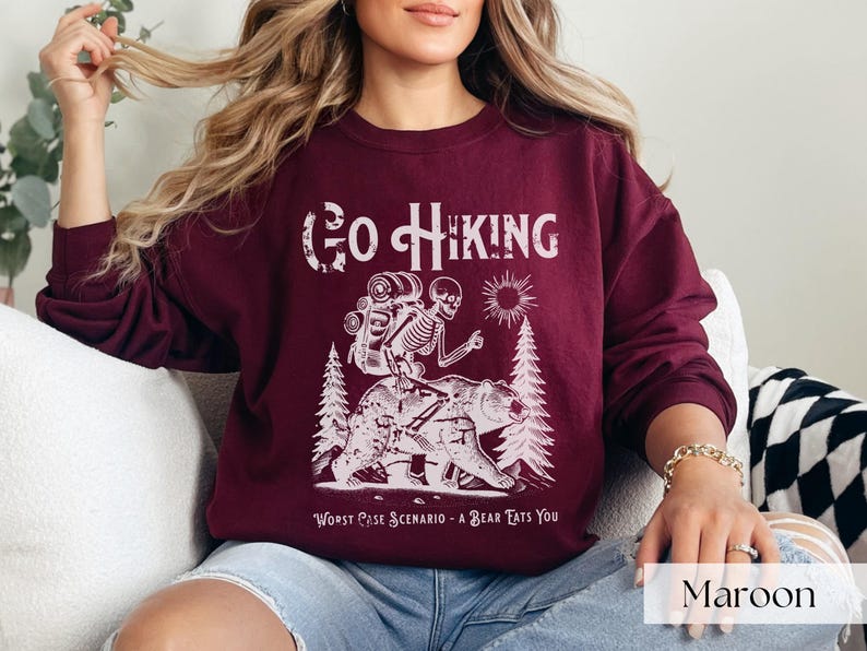 Woman wearing maroon Go Hiking Worst Case Scenario A Bear Kills You, Funny Camping Sweater featuring a skeleton on a bear. Perfect for outdoor enthusiasts and camper gifts. Ideal for Halloween and summer vacation.