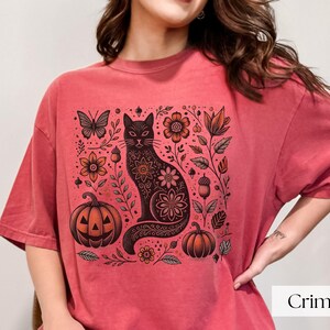 Woman wearing red Black Cat Halloween shirt featuring a spooky black cat, pumpkins, fall leaves, and flowers. Perfect for autumn and spooky season. Ideal for Halloween parties or as a cat lover gift with a vintage floral and witchy aesthetic.