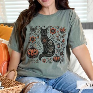 Woman wearing green Black Cat Halloween shirt featuring a spooky black cat, pumpkins, fall leaves, and flowers. Perfect for autumn and spooky season. Ideal for Halloween parties or as a cat lover gift with a vintage floral and witchy aesthetic.