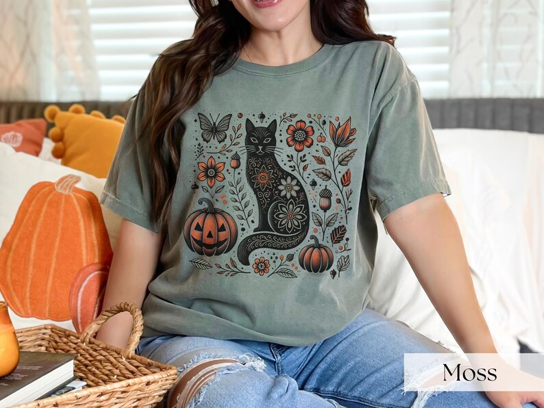 Woman wearing green Black Cat Halloween shirt featuring a spooky black cat, pumpkins, fall leaves, and flowers. Perfect for autumn and spooky season. Ideal for Halloween parties or as a cat lover gift with a vintage floral and witchy aesthetic.