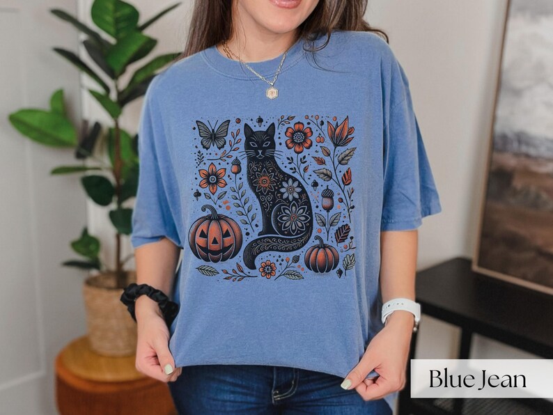 Woman wearing blue Black Cat Halloween shirt featuring a spooky black cat, pumpkins, fall leaves, and flowers. Perfect for autumn and spooky season. Ideal for Halloween parties or as a cat lover gift with a vintage floral and witchy aesthetic.