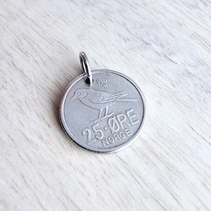 May include: Silver 25-øre coin from Norway with a bird design and the year 1969. The coin has a hole in the top for hanging.