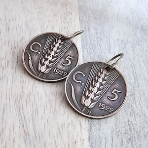 May include: Two antique coin pendants. Each circular pendant features a wheat stalk design, the number 5, and the year 1922. The pendants are made of a dark metal and have a small loop at the top for hanging.