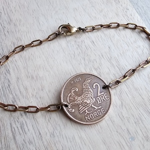 May include: A brass chain bracelet with a 1971 Norwegian 2 øre coin featuring a rooster design. The coin is attached to the chain with a metal ring.