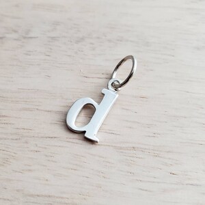 Dije de plata de ley con letra D minúscula recortada. Para añadir a collar o pulsera. Dije inicial con fuente serif. Ria Designs.