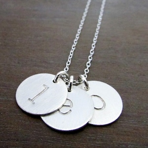 May include: A silver necklace with three round charms, each engraved with a letter. The letters are "I", "E", and "O".