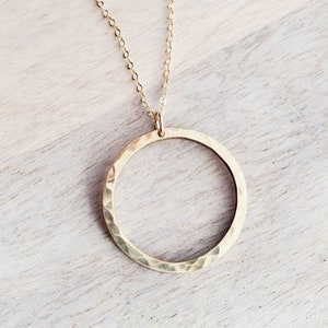May include: A gold hammered circle pendant necklace. The pendant is a large, open circle with a textured surface. The necklace is made of a delicate gold chain.